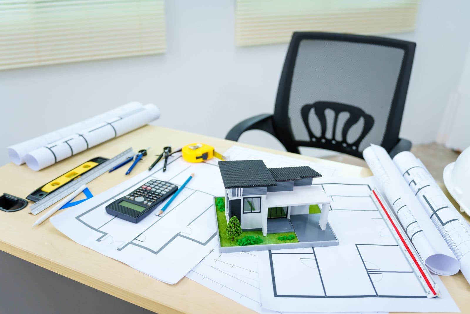 Scale house model, rolled drawings, and a calculator on an estimating desk.