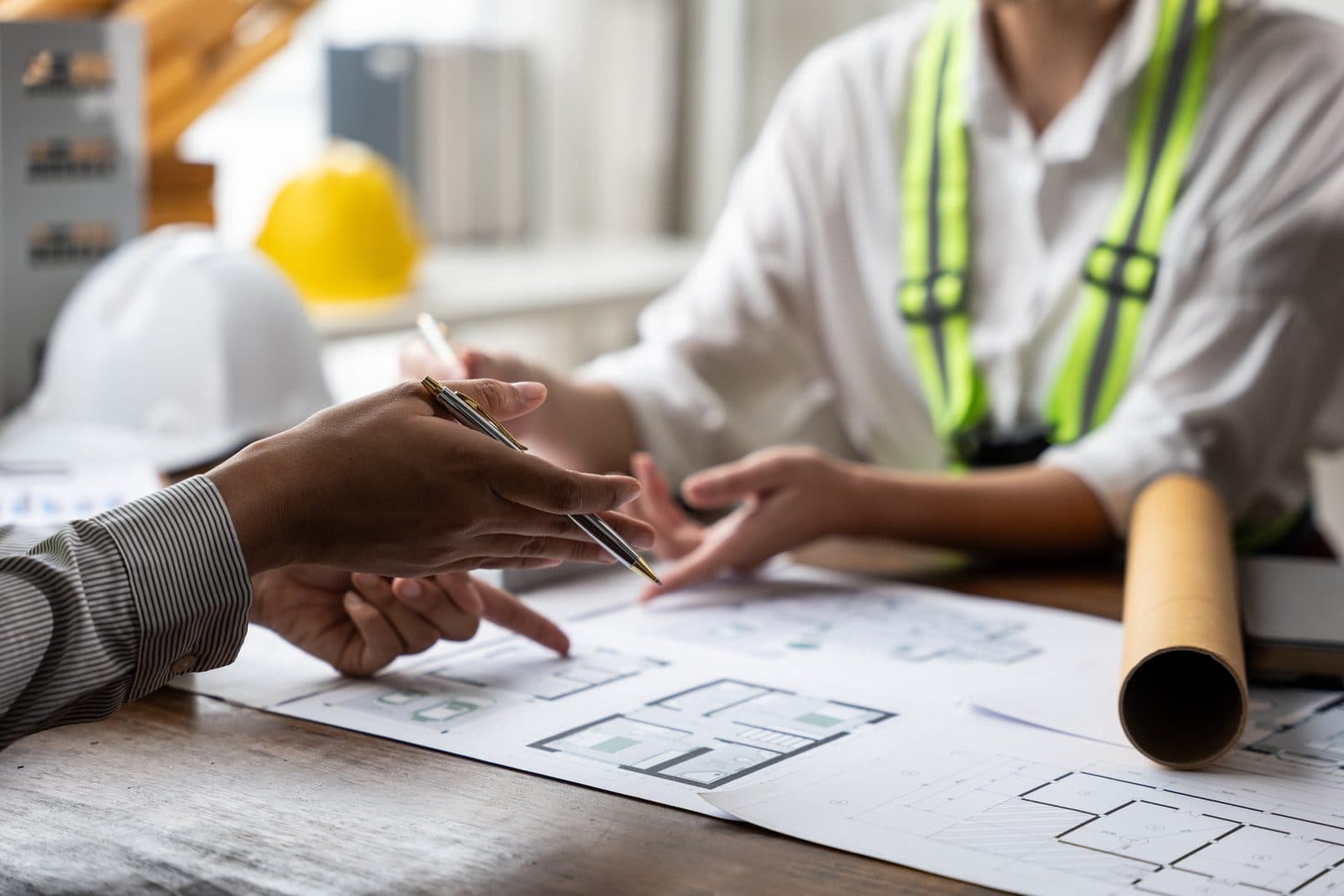 Hard hats, a safety vest, and floor plans on a review table.