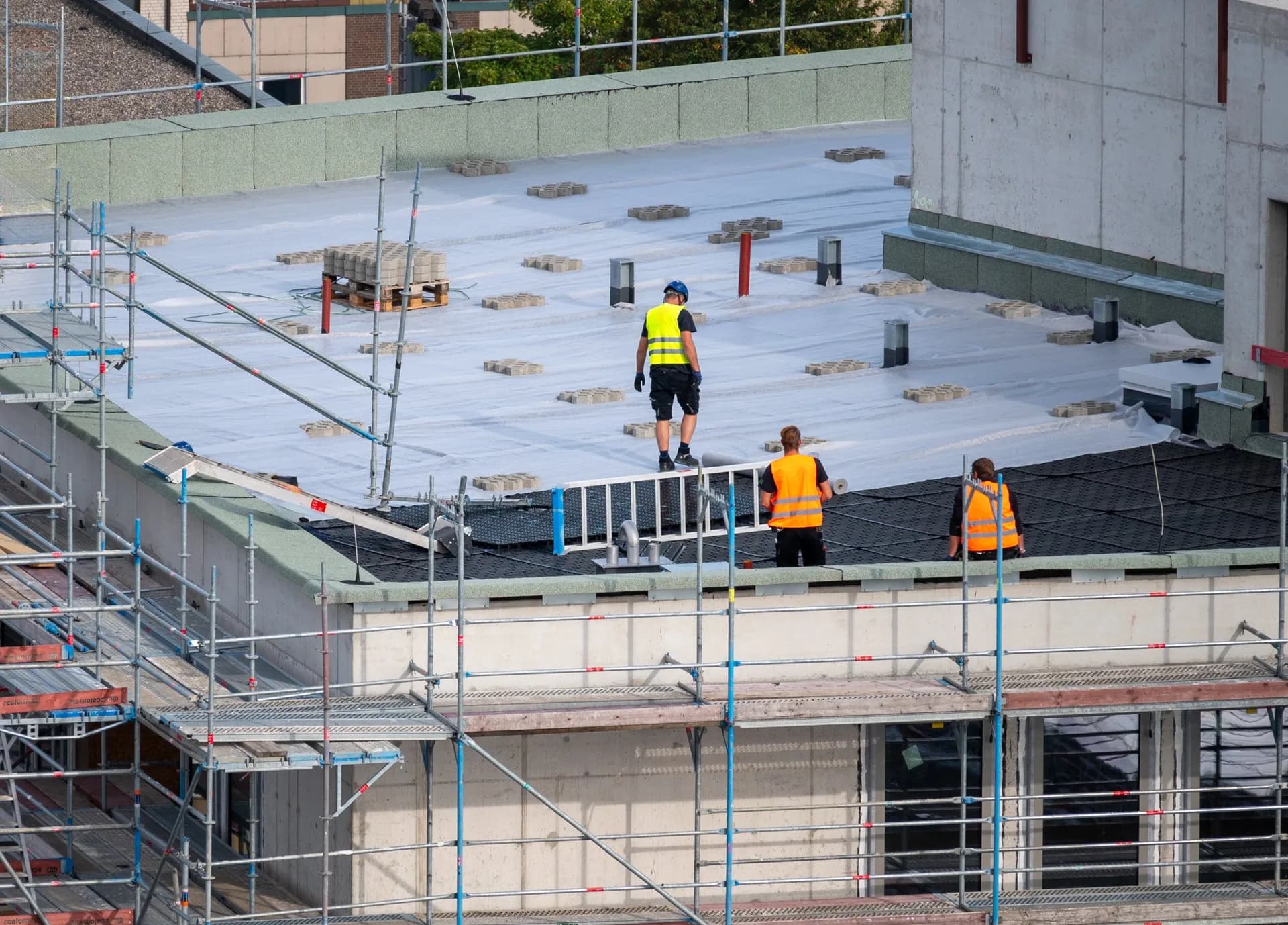 Commercial roofing crew installing membrane and drainage mats on a flat roof